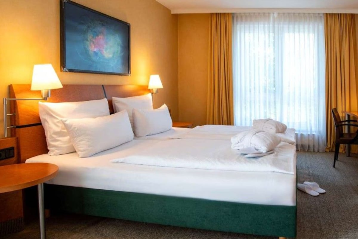 Une chambre d’hôtel avec un lit, deux lampes de chevet, un bureau, une chaise et un tableau au mur.