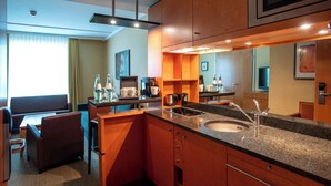 A modern hotel bathroom with a granite countertop, sink, and mirror. There is a seating area with a sofa and table, and a coffee machine.