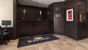 Un espace d’accueil d’hôtel avec un comptoir de réception en bois foncé, un écran d’ordinateur, une chaise et le logo de la chaîne Days Inn sur le sol.