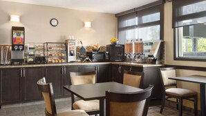 Un comptoir de cuisine avec une machine à café, un four à micro-ondes, un grille-pain et divers aliments. On y trouve des meubles en bois foncé, une horloge au mur et une fenêtre qui laisse entrer la lumière naturelle.