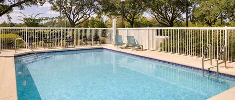 A rectangular swimming pool with clear blue water, surrounded by a white fence and trees.