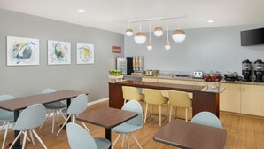 Un comedor moderno con una mesa larga, varias sillas, una encimera de cocina y una estación de café.