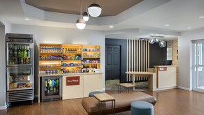 Un moderno vestíbulo de hotel con estación de bebidas de autoservicio, zona de estar y mostrador de recepción.