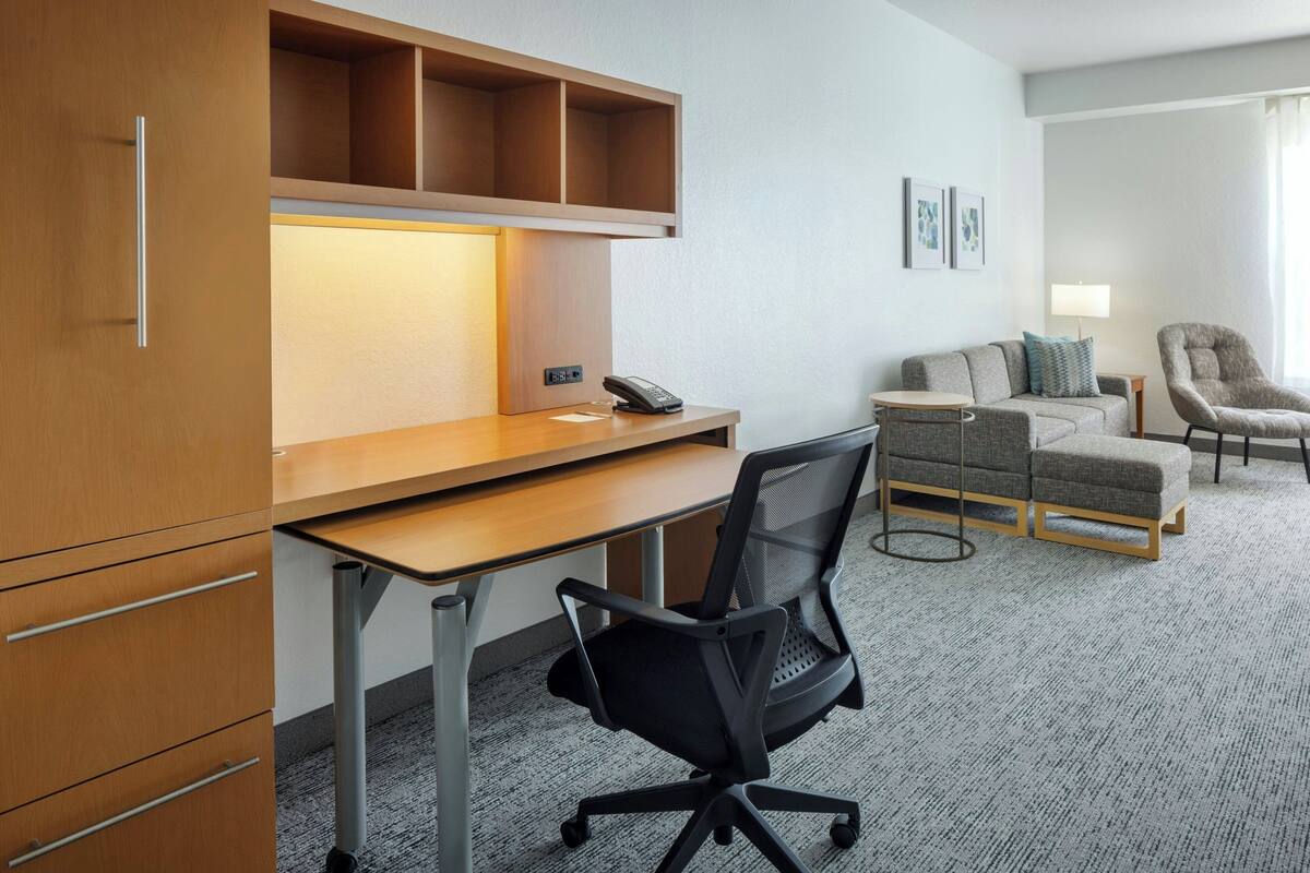 Una habitación de hotel con escritorio, silla de oficina, sofá y sillón.