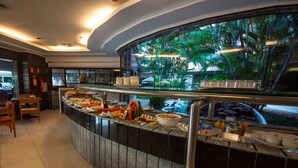 A buffet counter with various food items and a view of palm trees through a glass window.
