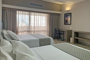 Habitación de hotel con dos camas, un escritorio, una silla y un amplio ventanal con cortinas.