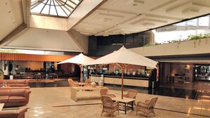 A spacious lobby with a high ceiling, a bar area, and seating arrangements including sofas and wicker chairs.