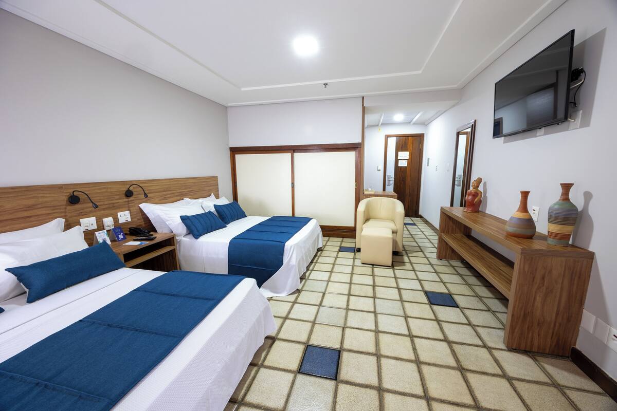 A hotel room with two beds, a sofa, a TV, and a wooden console table with decorative items.
