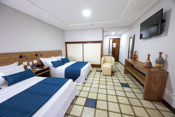 Habitación de hotel con dos camas, un sofá, un televisor y una consola de madera con objetos decorativos.