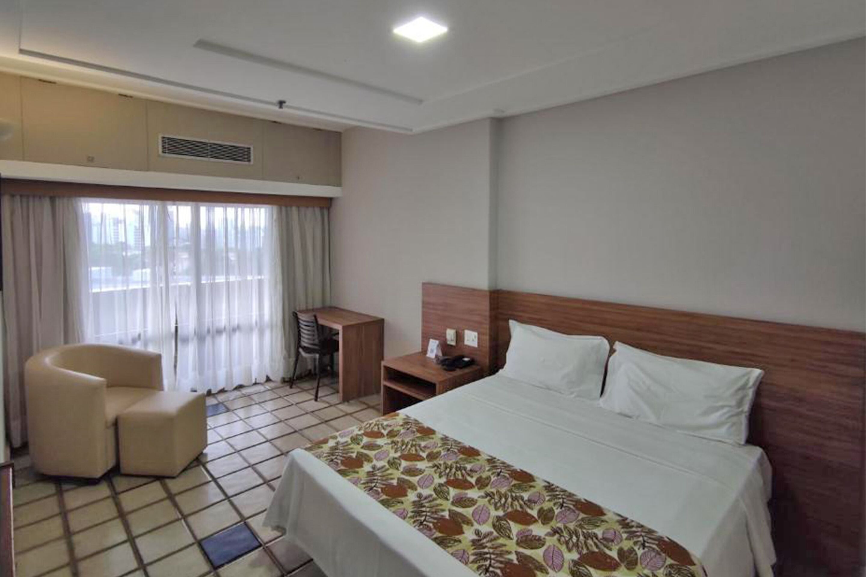 Een hotelkamer met een bed, een bureau, een stoel en een raam met gordijnen.