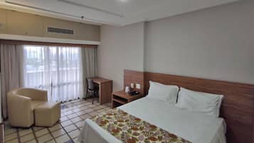 A hotel room with a bed, a desk, a chair, and a window with curtains.
