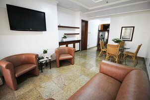 Una sala de estar con sofás de cuero, un televisor de pantalla plana, una zona de comedor con sillas de mimbre y una cocina al fondo.