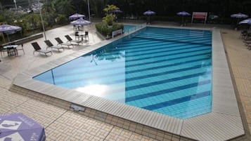 Piscina com bordas e deck azulejados. Cadeiras de descanso e guarda-sóis ao redor da piscina.