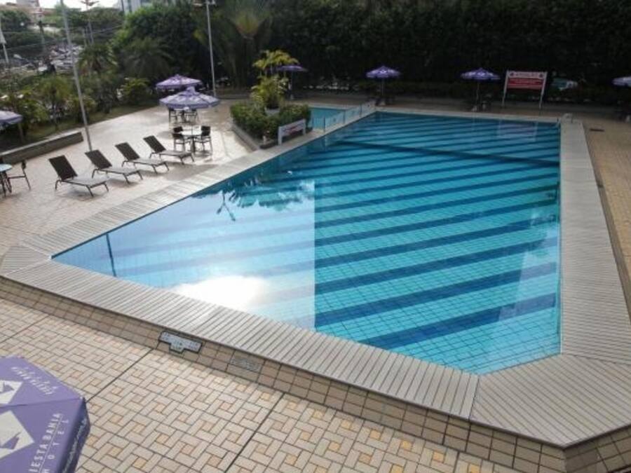 Piscina com bordas e deck azulejados. Cadeiras de descanso e guarda-sóis ao redor da piscina.