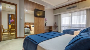 A hotel room with two beds, a TV, a dining area, and a bathroom.