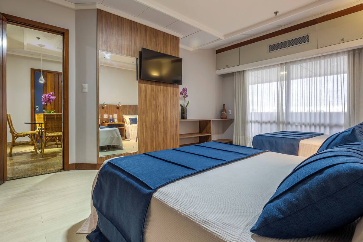 A hotel room with two beds, a TV, a dining area, and a bathroom.