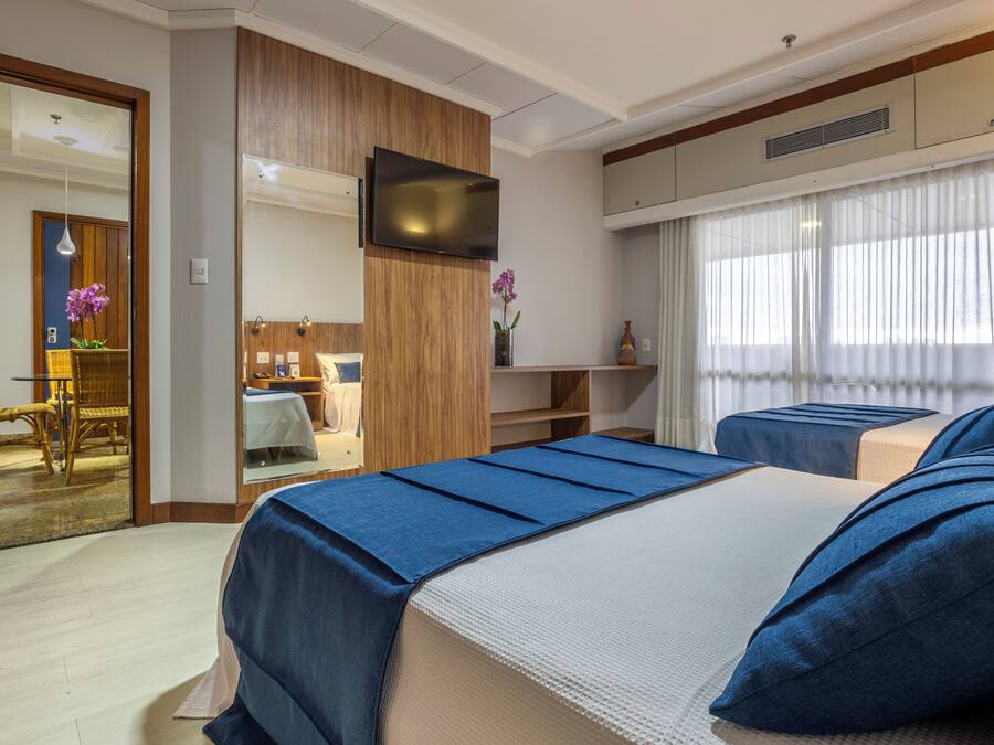 A hotel room with two beds, a TV, a dining area, and a bathroom.