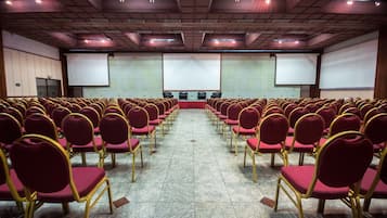 Uma sala de conferências com fileiras de cadeiras vermelhas e uma tela grande na frente.