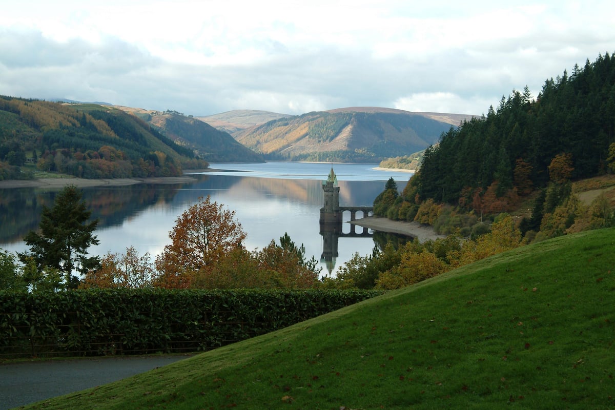 A serene lake with a tower in the center, surrounded by rolling hills and autumn foliage.