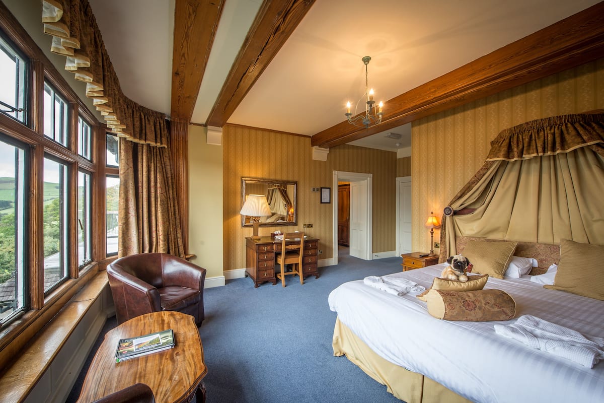 A hotel room with a large bed, a desk with a chair, a wooden table, and a window with curtains.