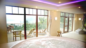 Un cuarto de spa con hidromasaje, sillas de madera y ventanas amplias con vistas al exterior.