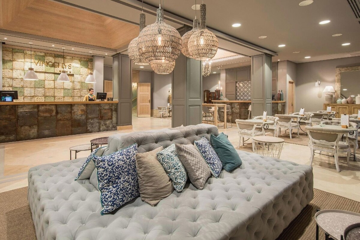 Un hall de hotel con mostrador de recepción, zona de estar y un amplio sofá capitonado con cojines estampados.
