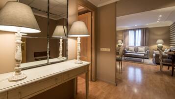Habitación de hotel con piso de madera, un sofá, una mesa de comedor y un espejo que refleja el espacio.