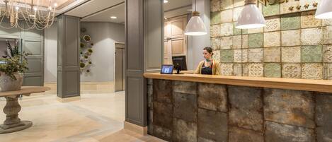 A reception area with a wooden counter, a receptionist, and a decorative wall with a name sign.