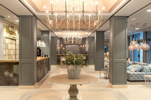A spacious lobby with a central round table, a chandelier, and a seating area with a sofa and chairs. - Vincci Lys Hotel (Valencia)
