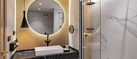 A modern bathroom with a black marble sink, a large mirror, and a glass-enclosed shower.