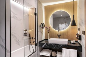Een moderne badkamer met een glazen douchecabine, een betegelde muur van marmer, een houten paneeldecoratie, een ronde spiegel en een zwart hanglampje.