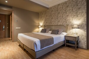 Una cama bien hecha con cabecera, dos mesitas de noche con lámparas y una pared con diseño de piedra.
