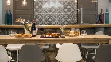 Un espace bar avec un comptoir en bois, des chaises blanches et grises, et des bouteilles de vin.