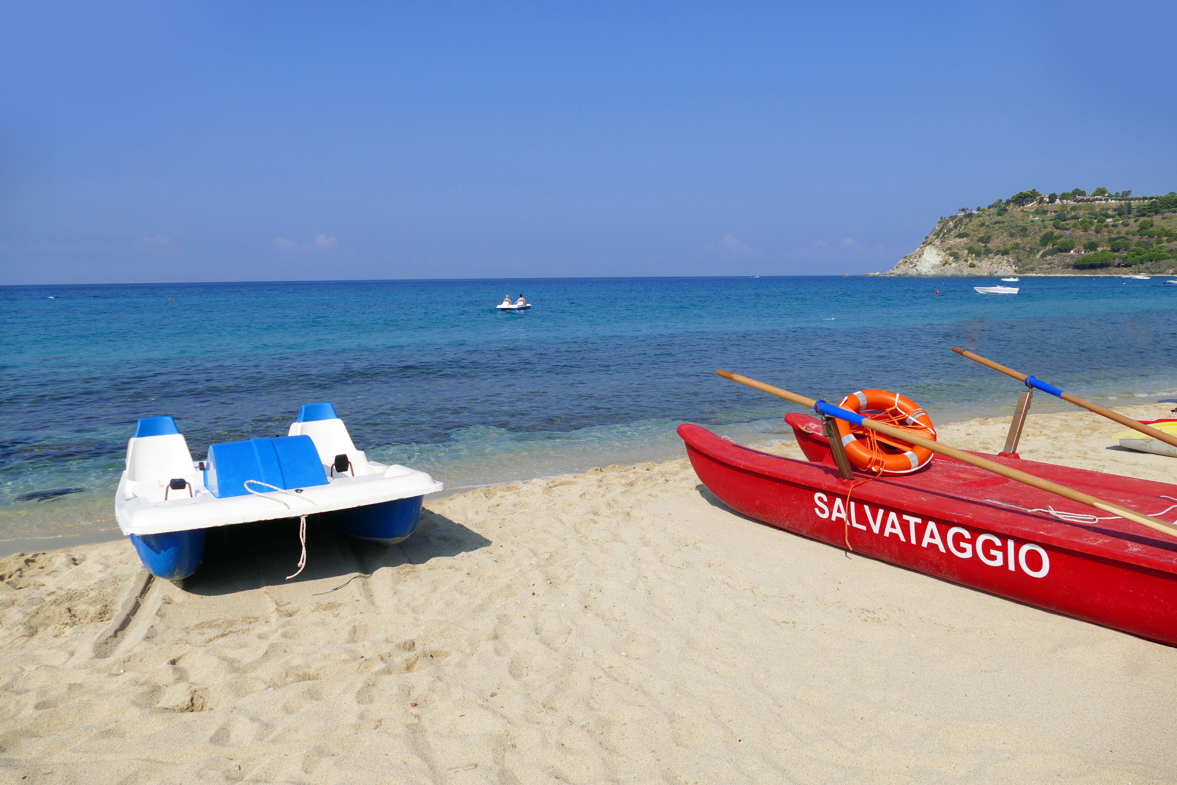 A beach with two boats, one blue and white, and one red with "SALVATAGGIO" written on it.
