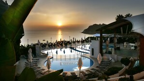 A pool area with lounge chairs and umbrellas, surrounded by a building with a curved roof. - Scoglio della Galea Village & Spa (Ricadi)