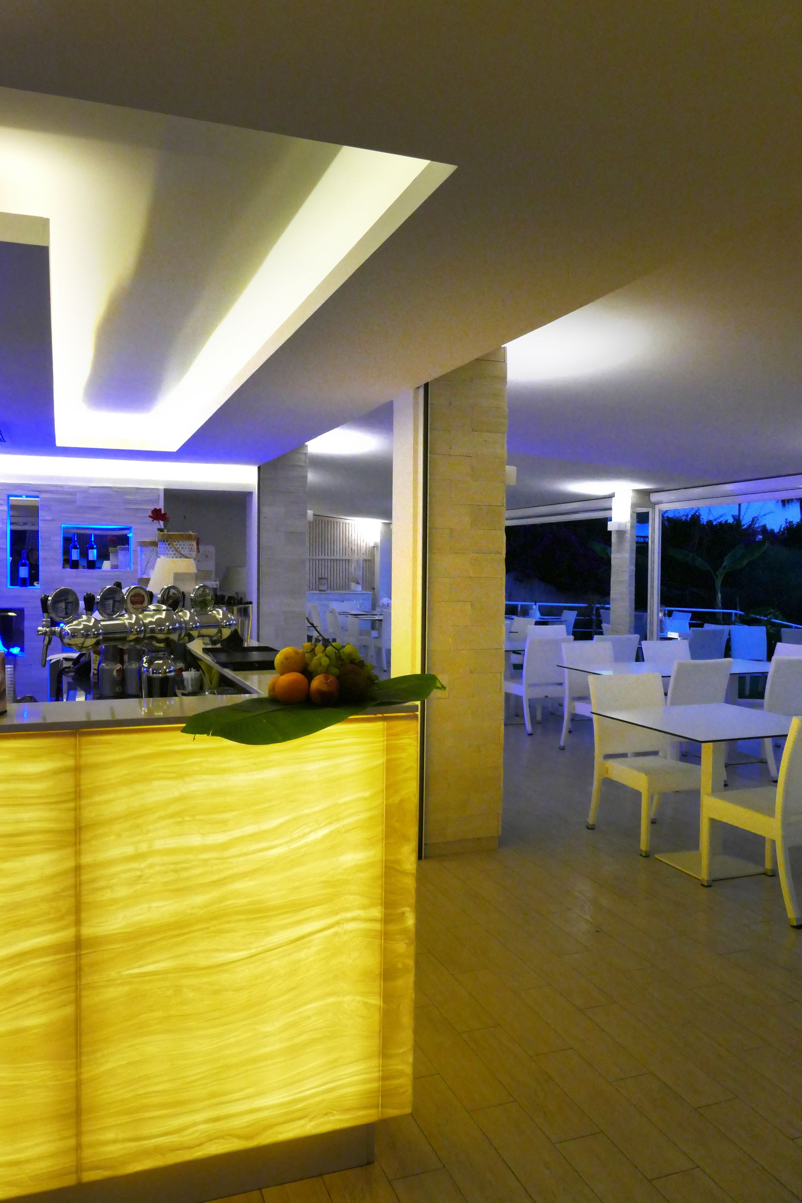 Un área de bar moderna con mostrador, taburetes y una zona de estar con mesas y sillas.