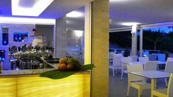 Un área de bar moderna con mostrador, taburetes y una zona de estar con mesas y sillas.