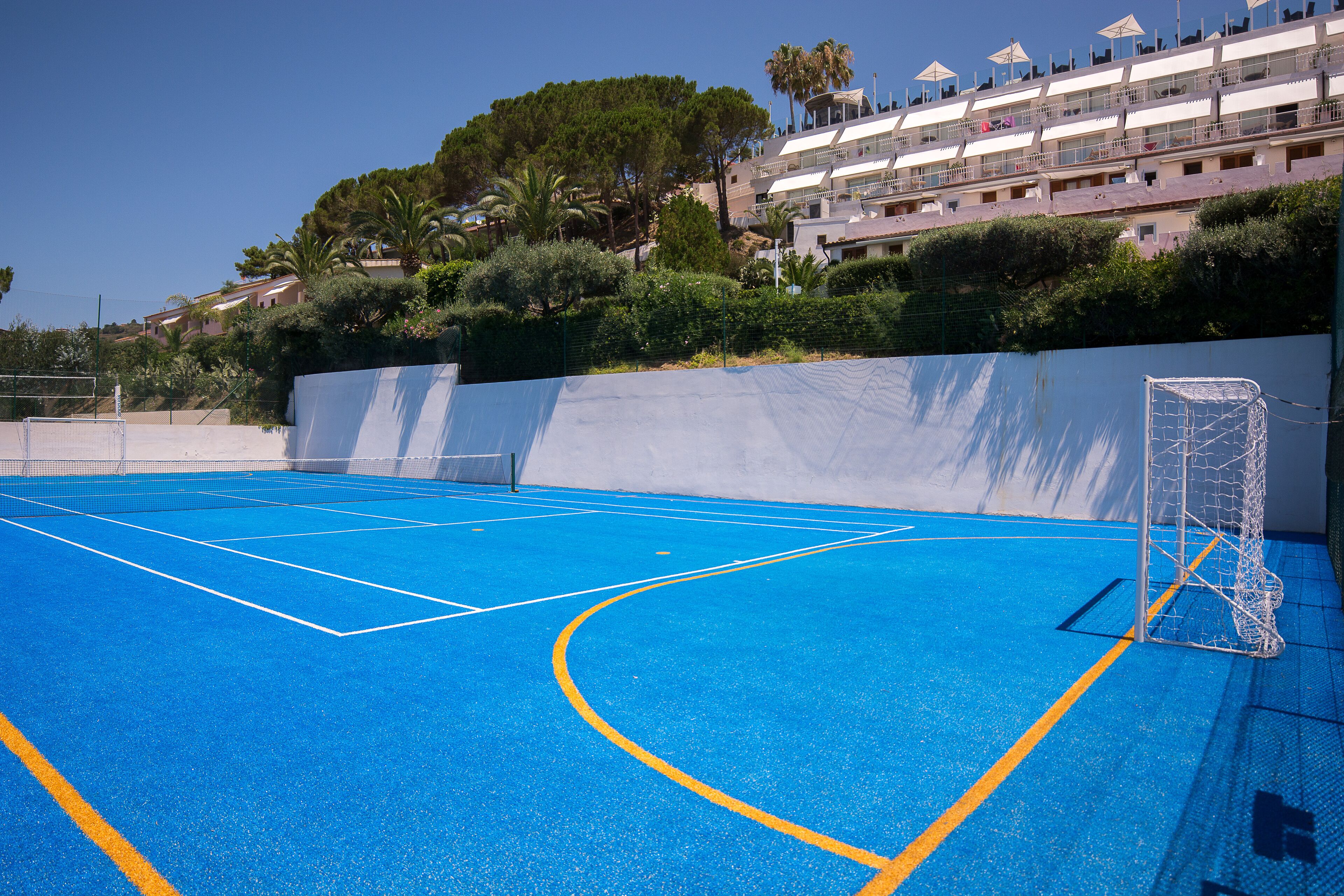 Cancha de tenis al aire libre con un arco, rodeada de césped y vegetación.