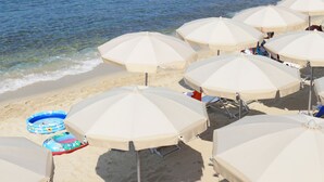 A beach with multiple white umbrellas, a clear blue sea, and a rocky hill in the background. - Scoglio della Galea Village & Spa (Ricadi)