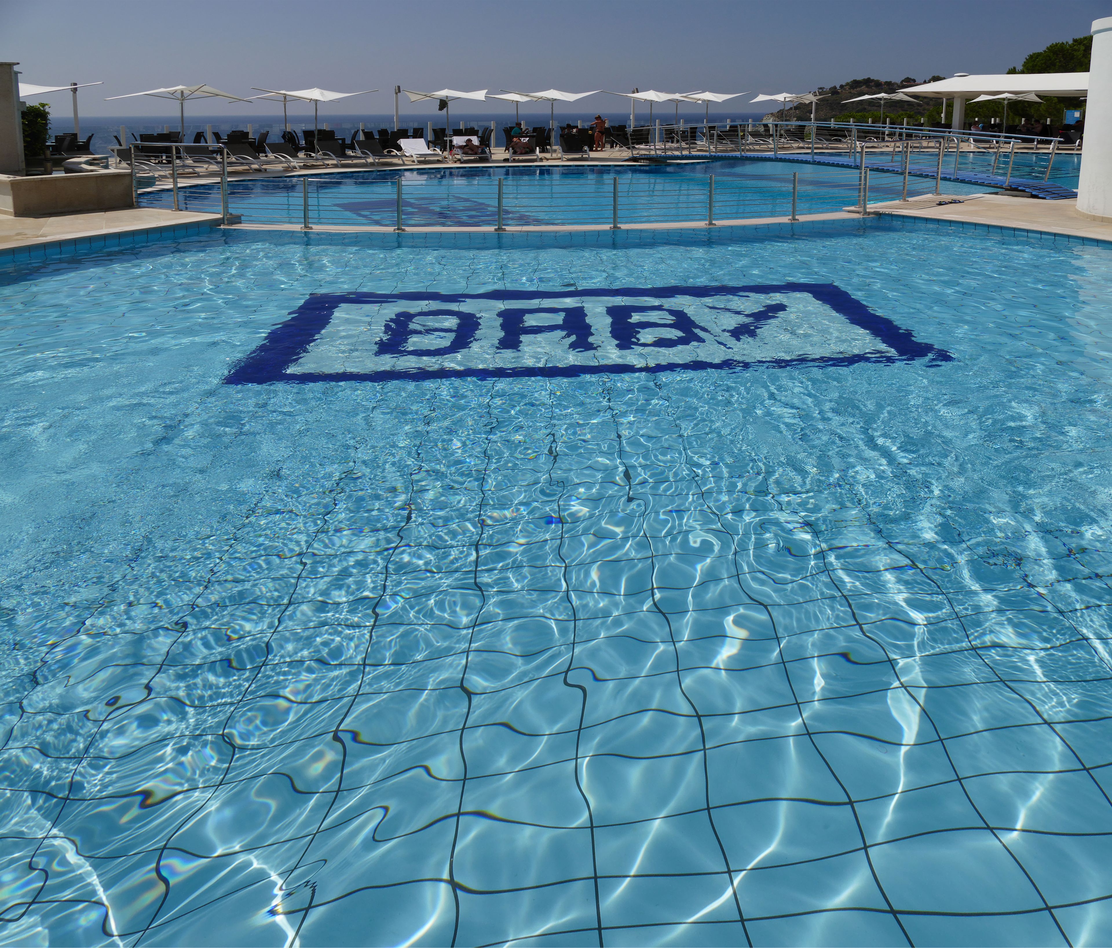 A swimming pool with a clear water surface and a poolside area with lounge chairs and umbrellas.