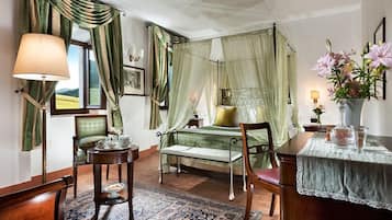 Un dormitorio con cama a dosel, una mesita de noche con lámpara, una silla, una pequeña mesa con un jarrón de flores y vistas al exterior.