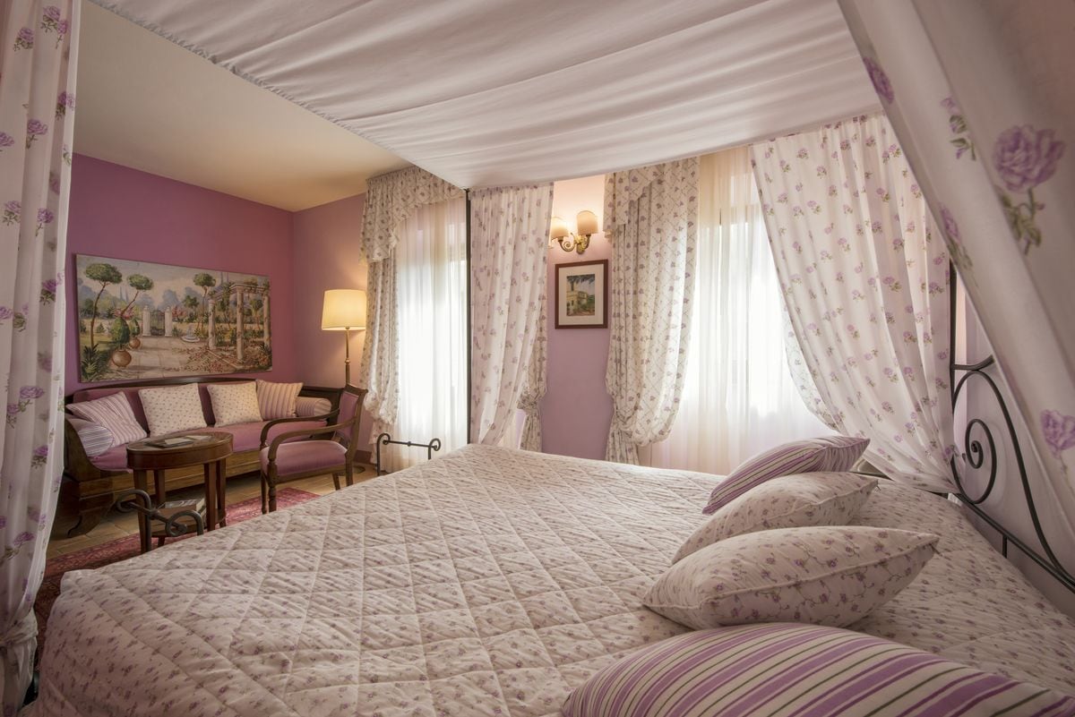 A bedroom with a large bed, a sofa, a small table, and a painting on the wall.