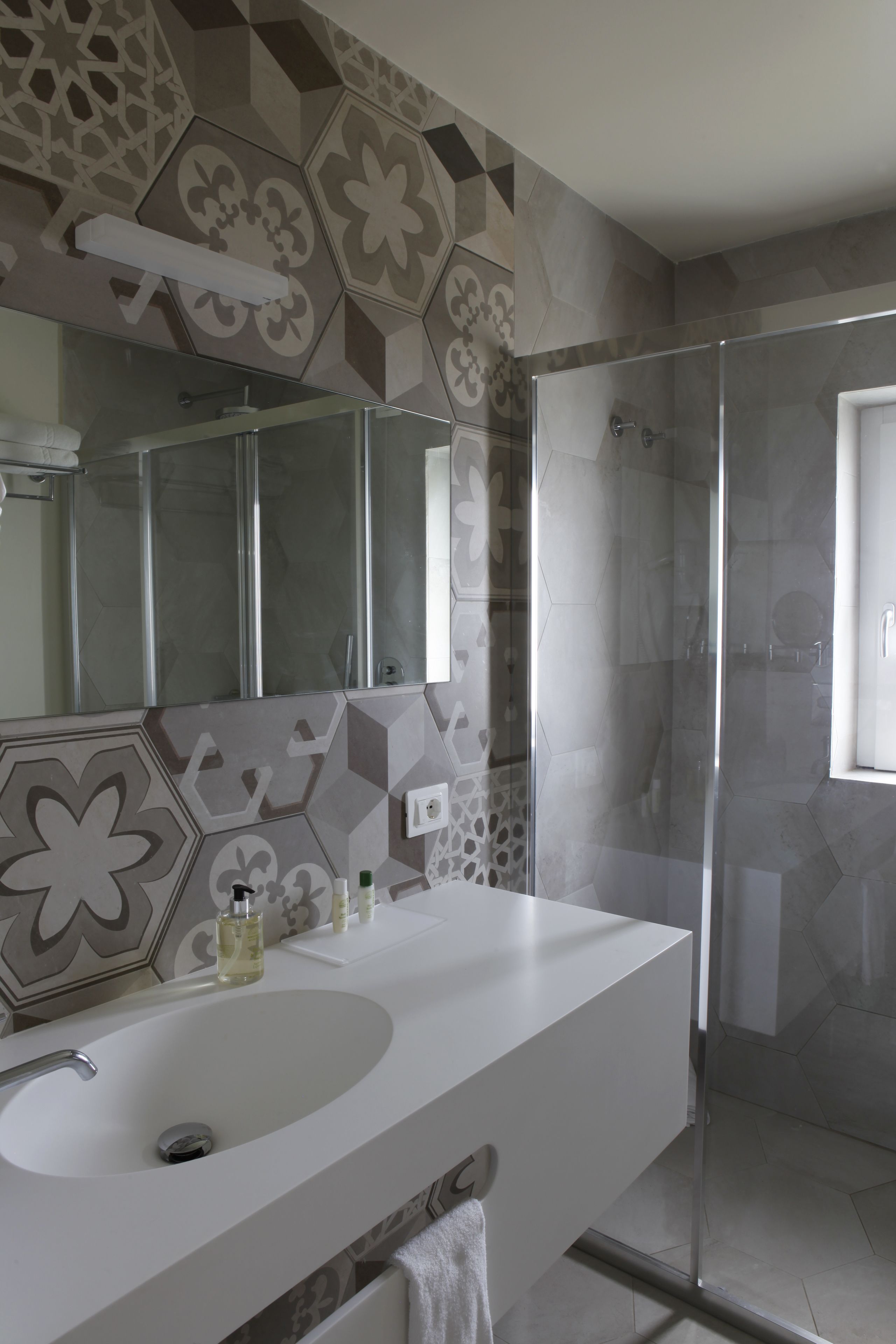 A bathroom with a white sink, a glass shower enclosure, and patterned tiles on the walls.