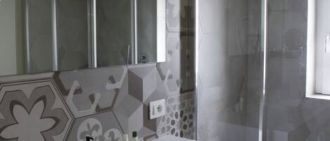 A bathroom with a white sink, a glass shower enclosure, and patterned tiles on the walls.