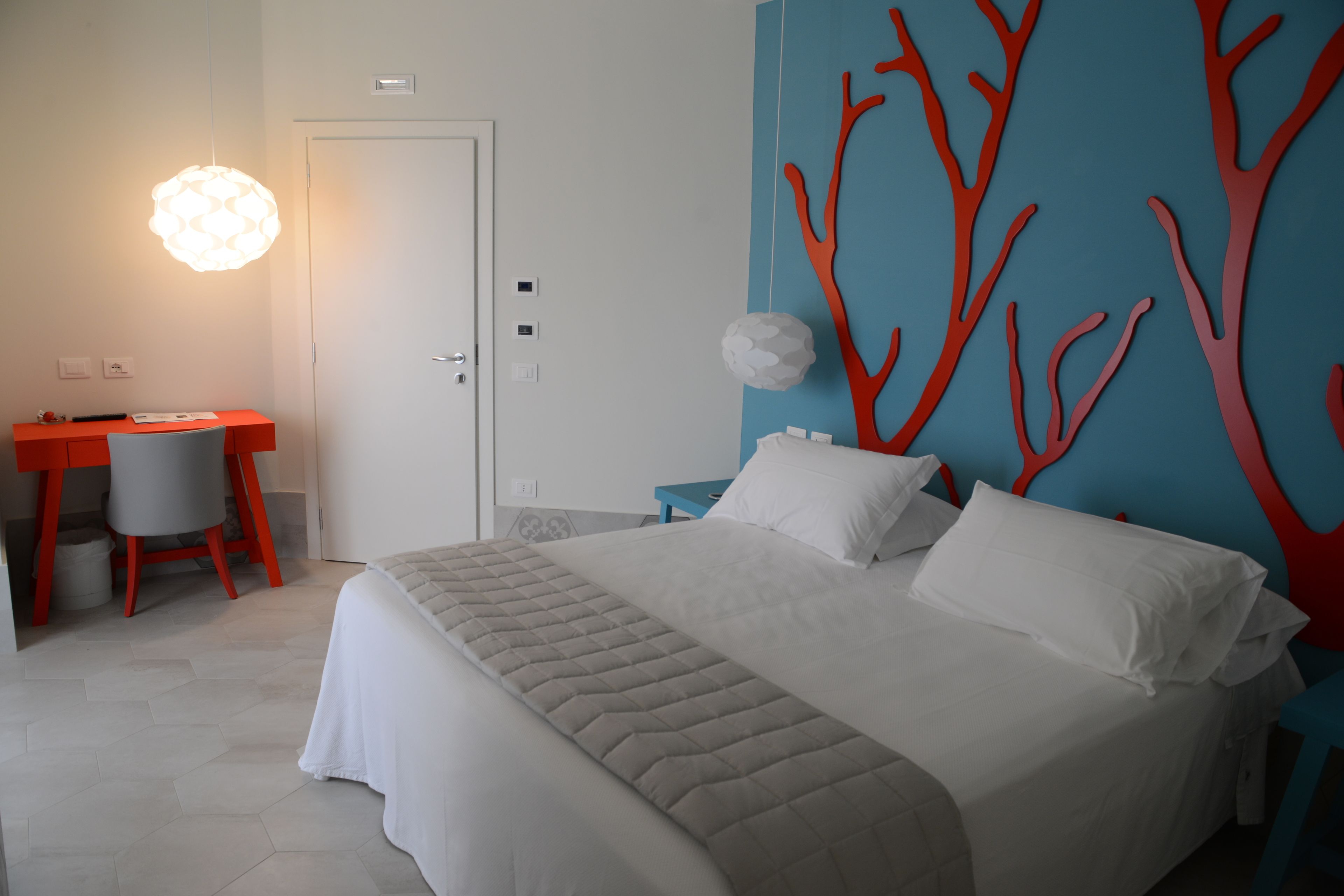 Una camera da letto moderna con un letto grande, una scrivania con una sedia e una parete decorata con motivi simili ad alberi rossi.