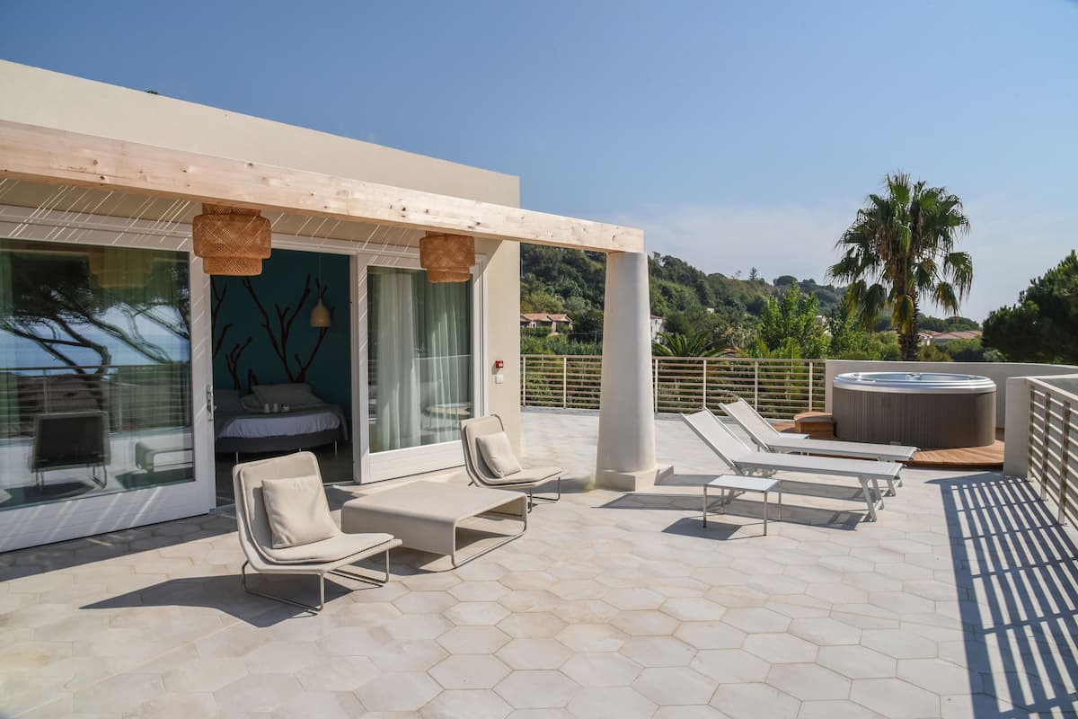 A modern outdoor lounge area with hexagonal tiles, lounge chairs, a hot tub, and a view of the surrounding landscape.