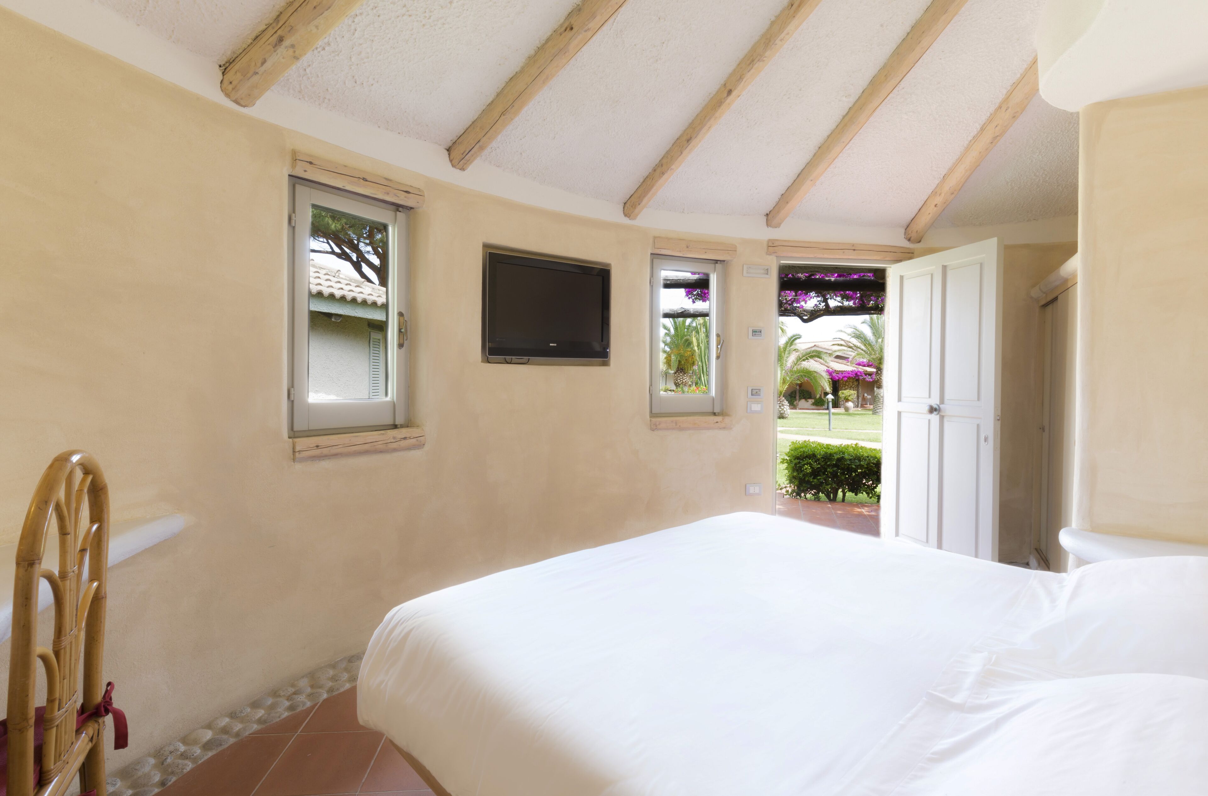 A bedroom with a bed, a television mounted on the wall, and a door leading to an outdoor area.
