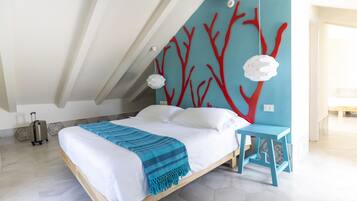 Un dormitorio con una cama, una silla azul, una maleta y una pared decorada con motivos de árboles rojos.