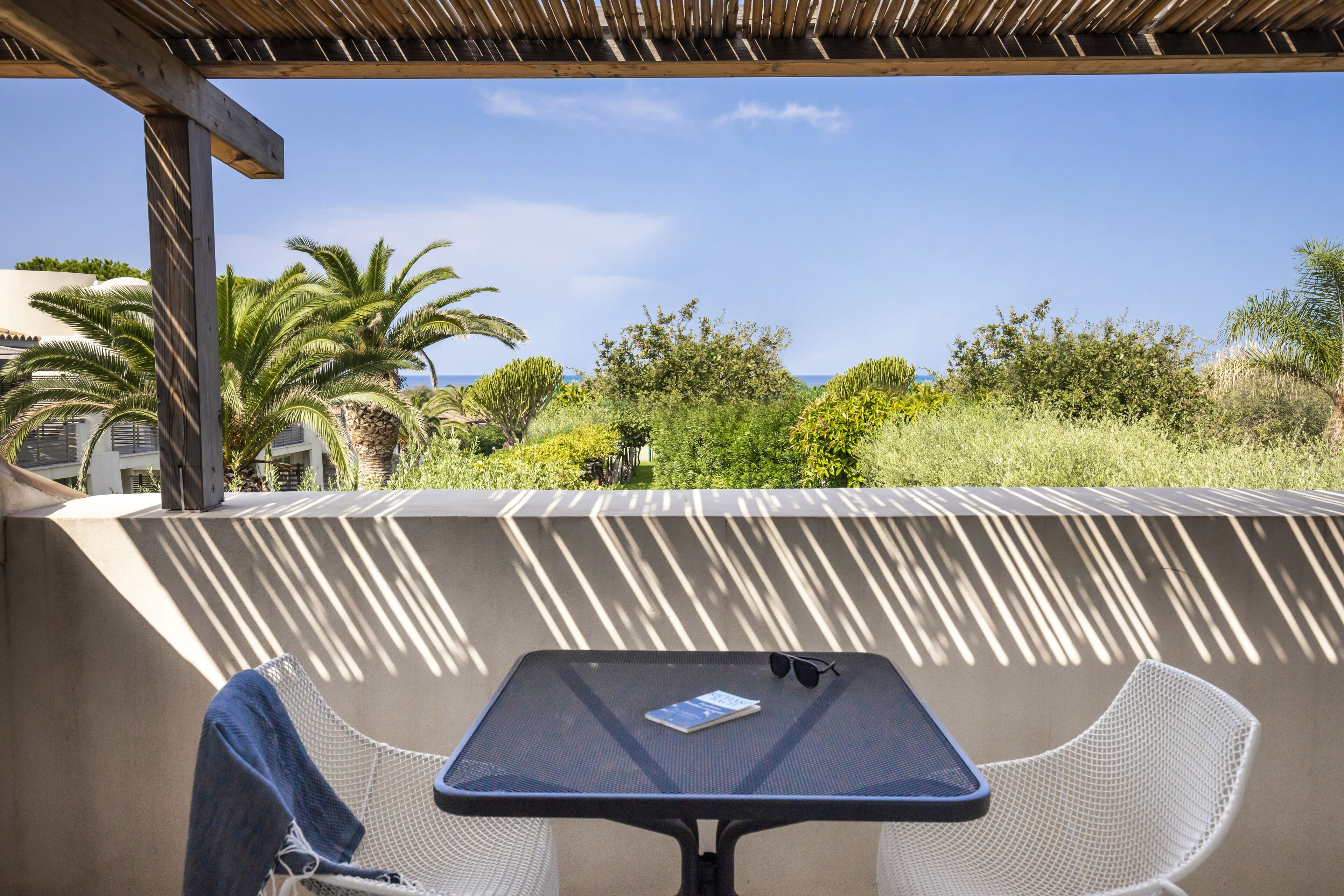 Un espacio de estar al aire libre cubierto, con mesa y sillas, que da a un jardín y vistas al mar.