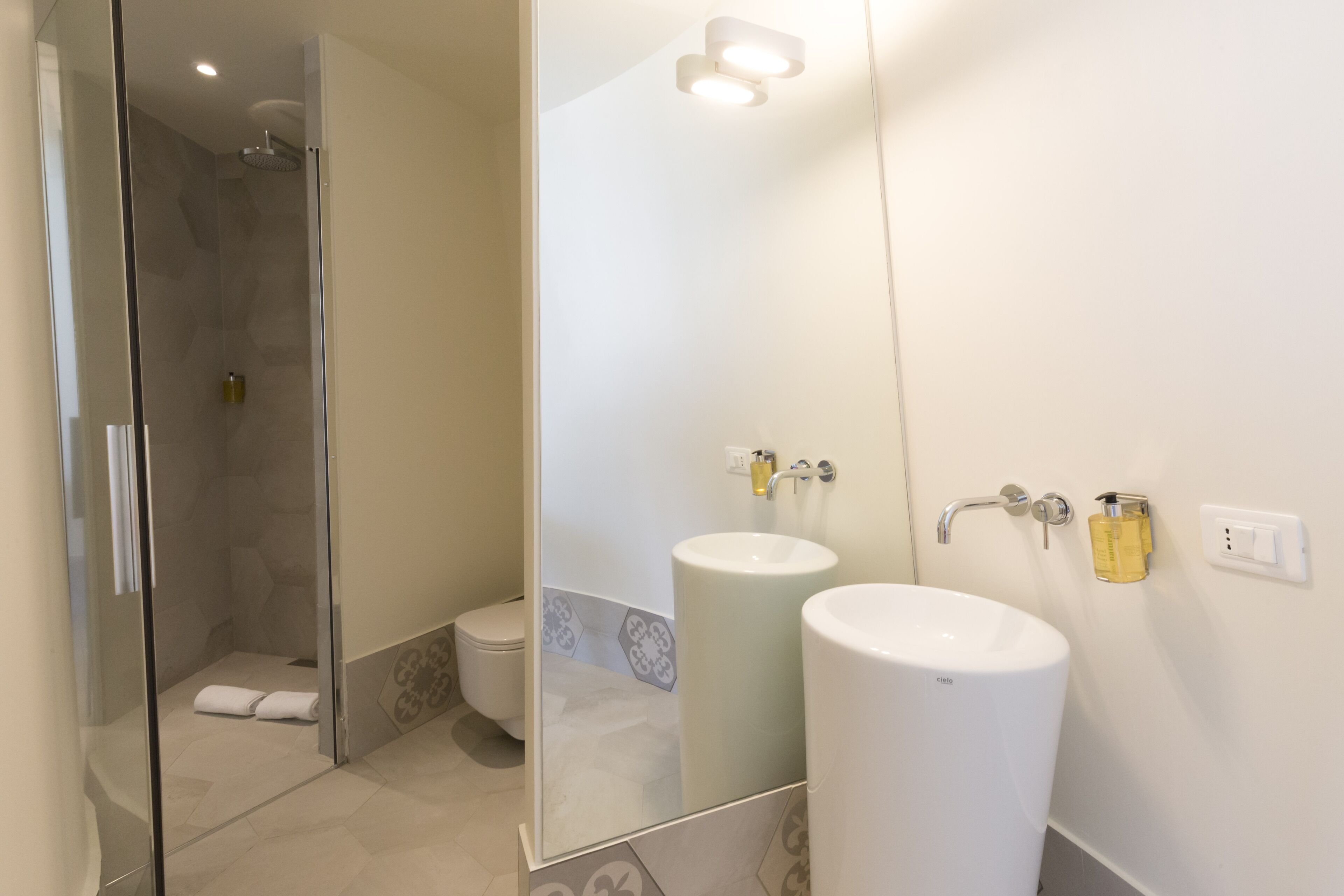 Un baño moderno con cabina de ducha de vidrio, dos lavabos y un espejo grande.